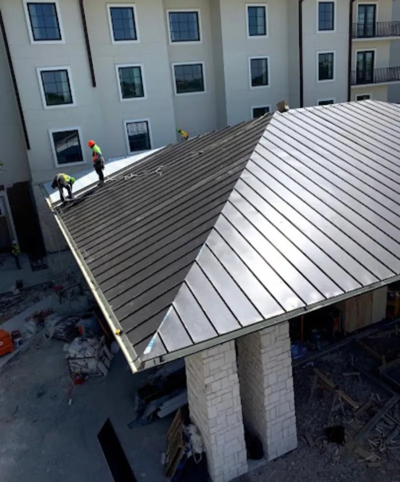 Crew installing standing seam metal roof panels on a commercial project in Burton